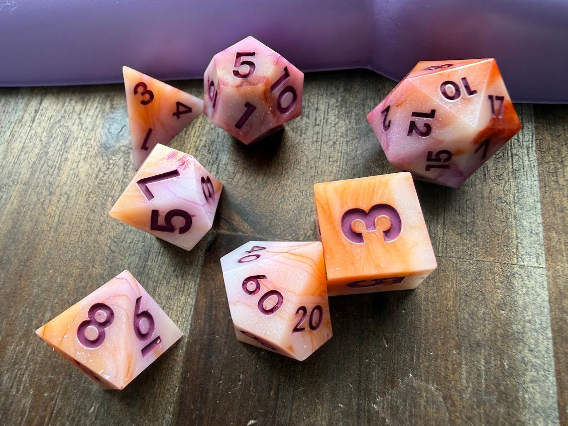 Set of pink and orange polyhedral dice on a wooden surface