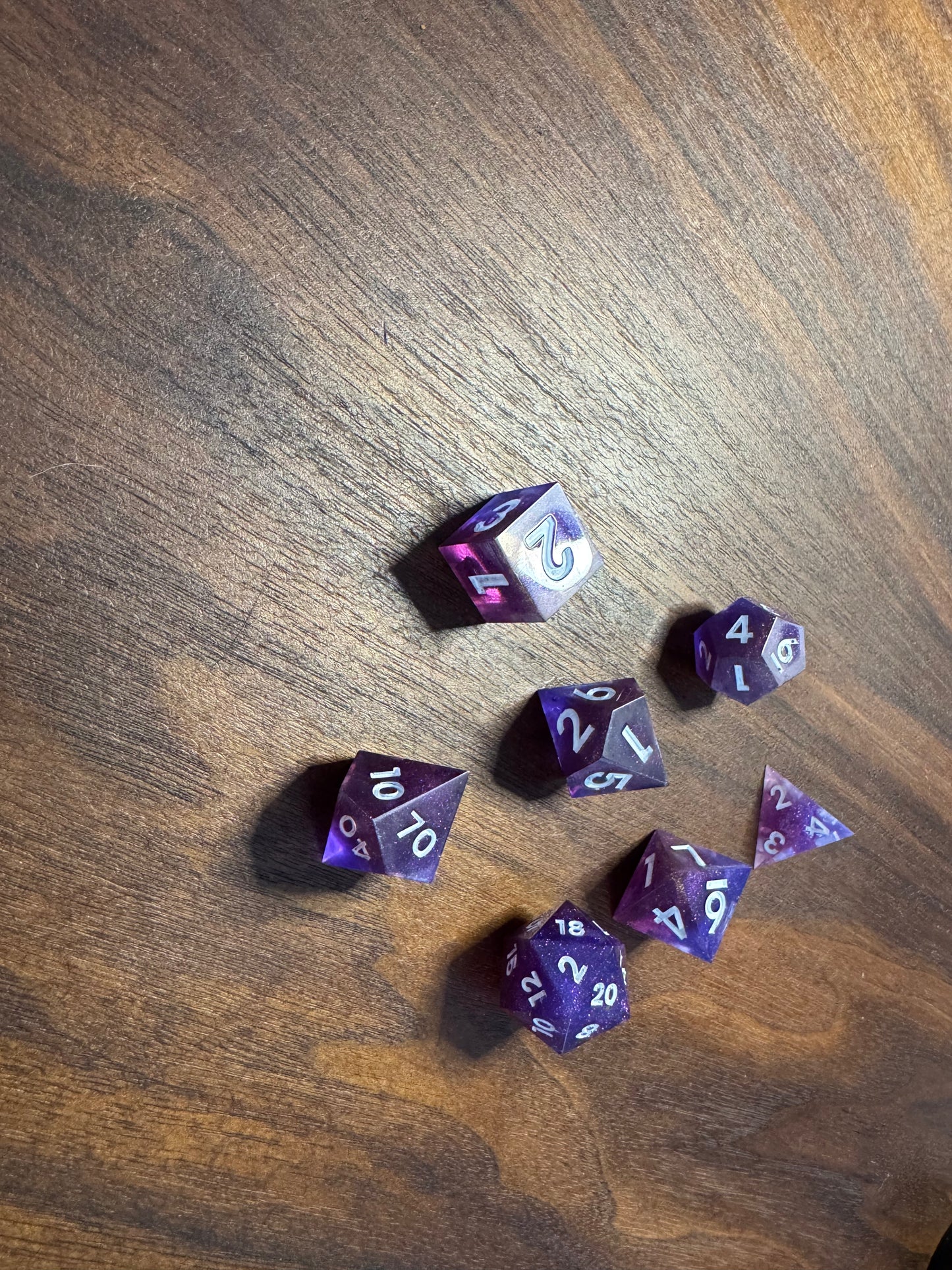 polyhedral sharp-edge, a set of seven in blue and purple on a wood able. Numbers are inked in white.