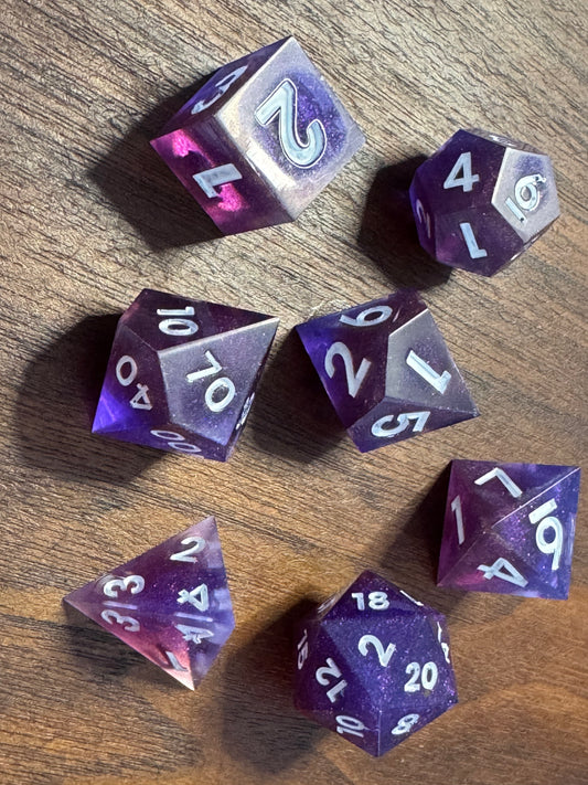 polyhedral sharp-edge, a set of seven in blue and purple on a wood table. Numbers are inked in white.