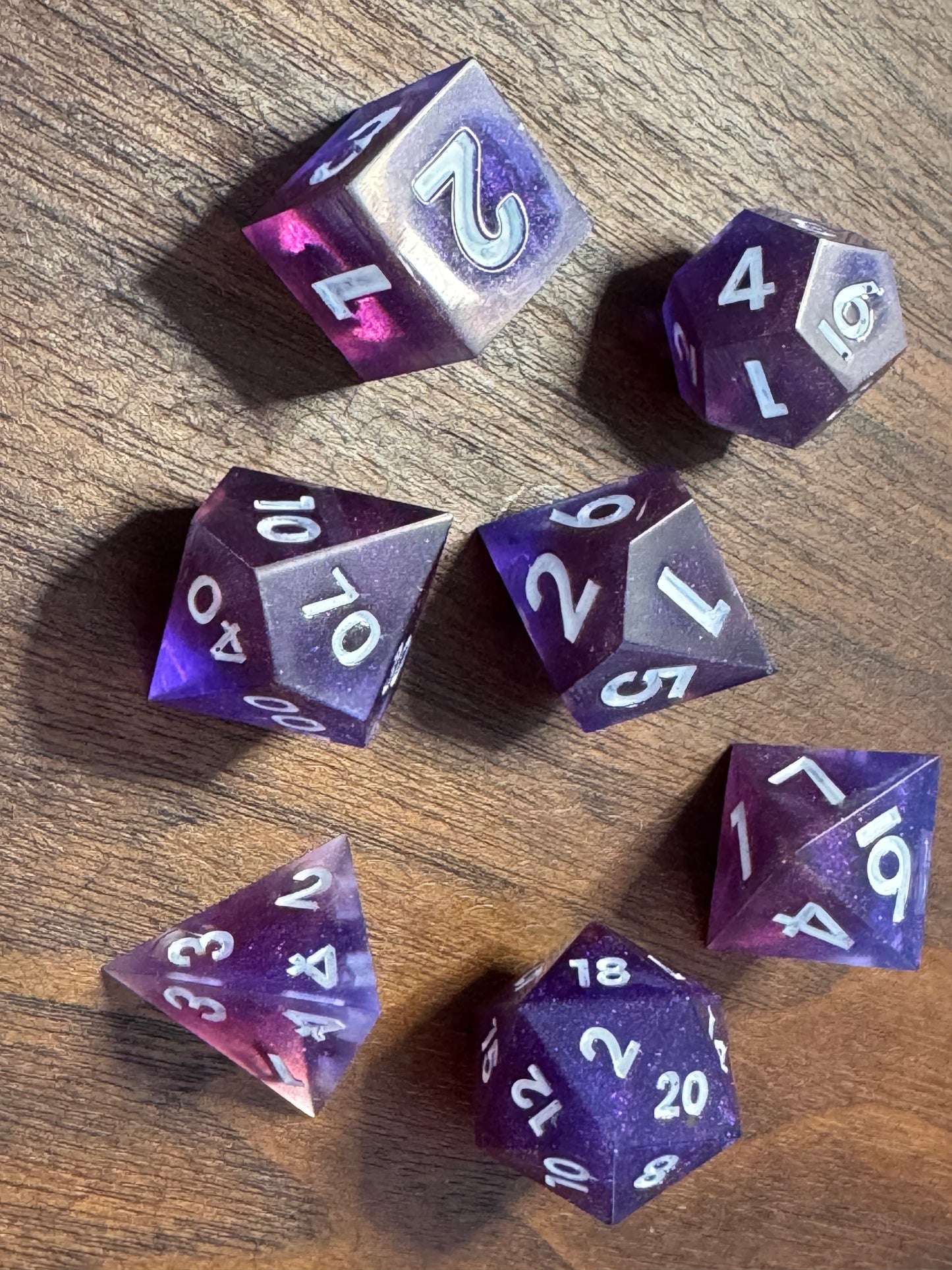 polyhedral sharp-edge, a set of seven in blue and purple on a wood able. Numbers are inked in white.