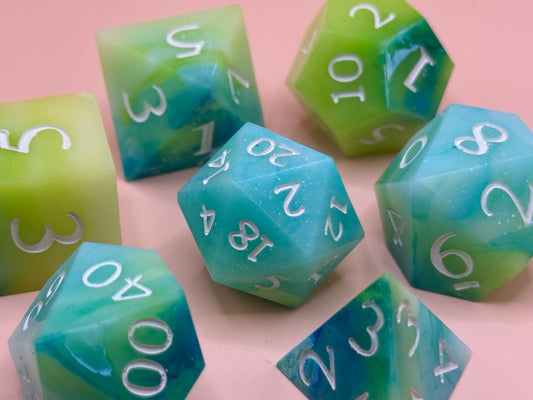 A set of seven green, blue and white dice on a pink surface.