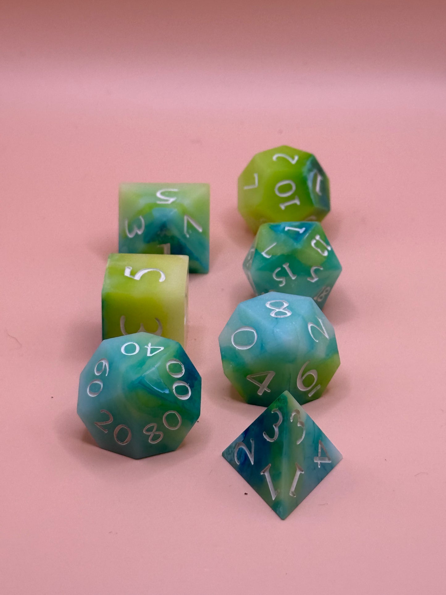 A set of seven green, blue and white dice on a pink surface.