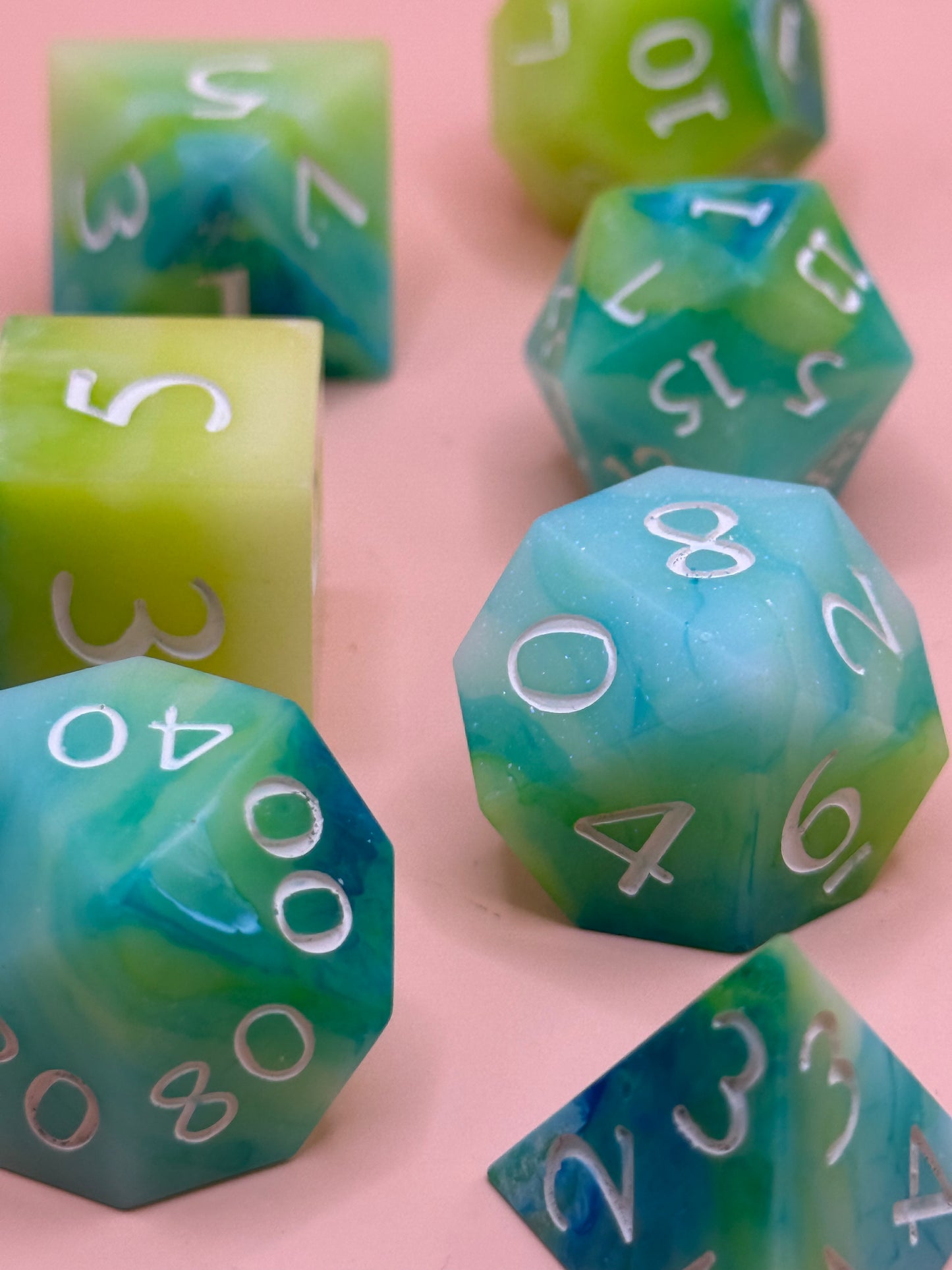 A set of seven green, blue and white dice on a pink surface.
