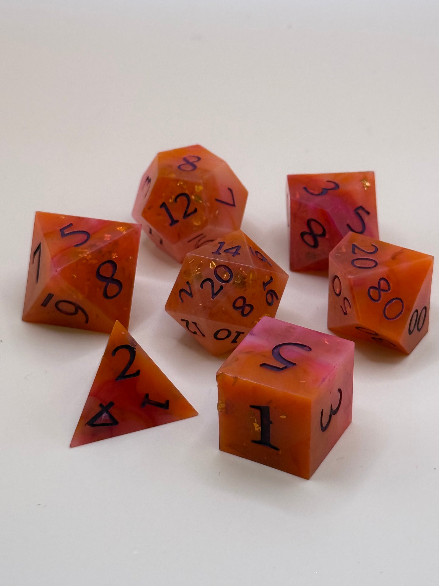 A set of 7 orange and red, swirled polyhedral dice on a table.