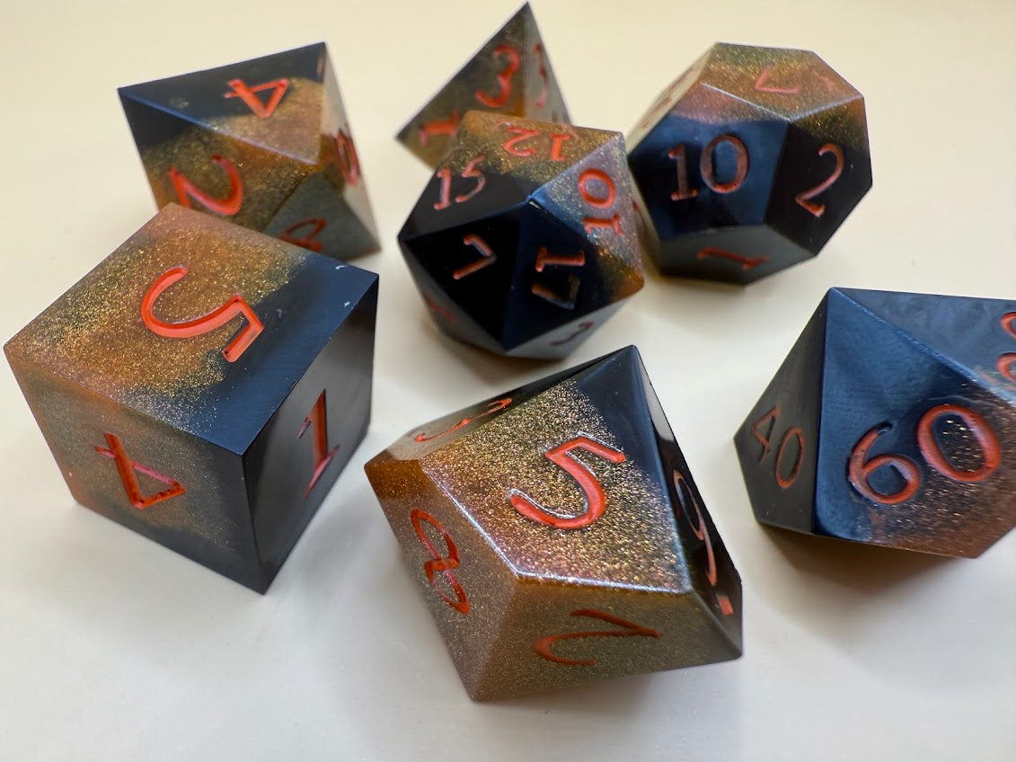 Set of black and gold polyhedral dice with metallic sheen on a white background