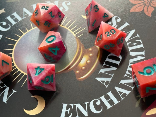 Pink and red polyhedral dice on a dark surface with 'Enchanted' text
