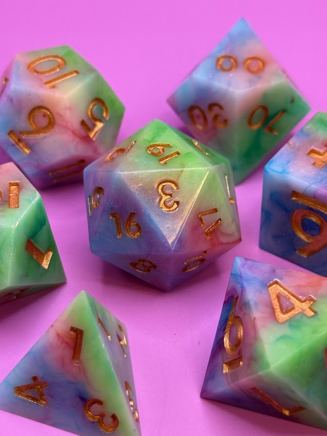Colorful polyhedral dice with gold numbers on a pink background
