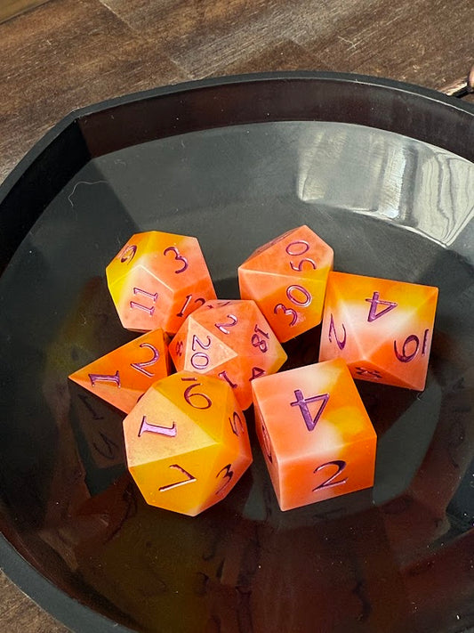 Set of orange polyhedral dice with purple numbers on a dark surface