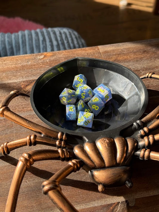 Blue dice with yellow markings in a black dish on a spider-shaped stand.