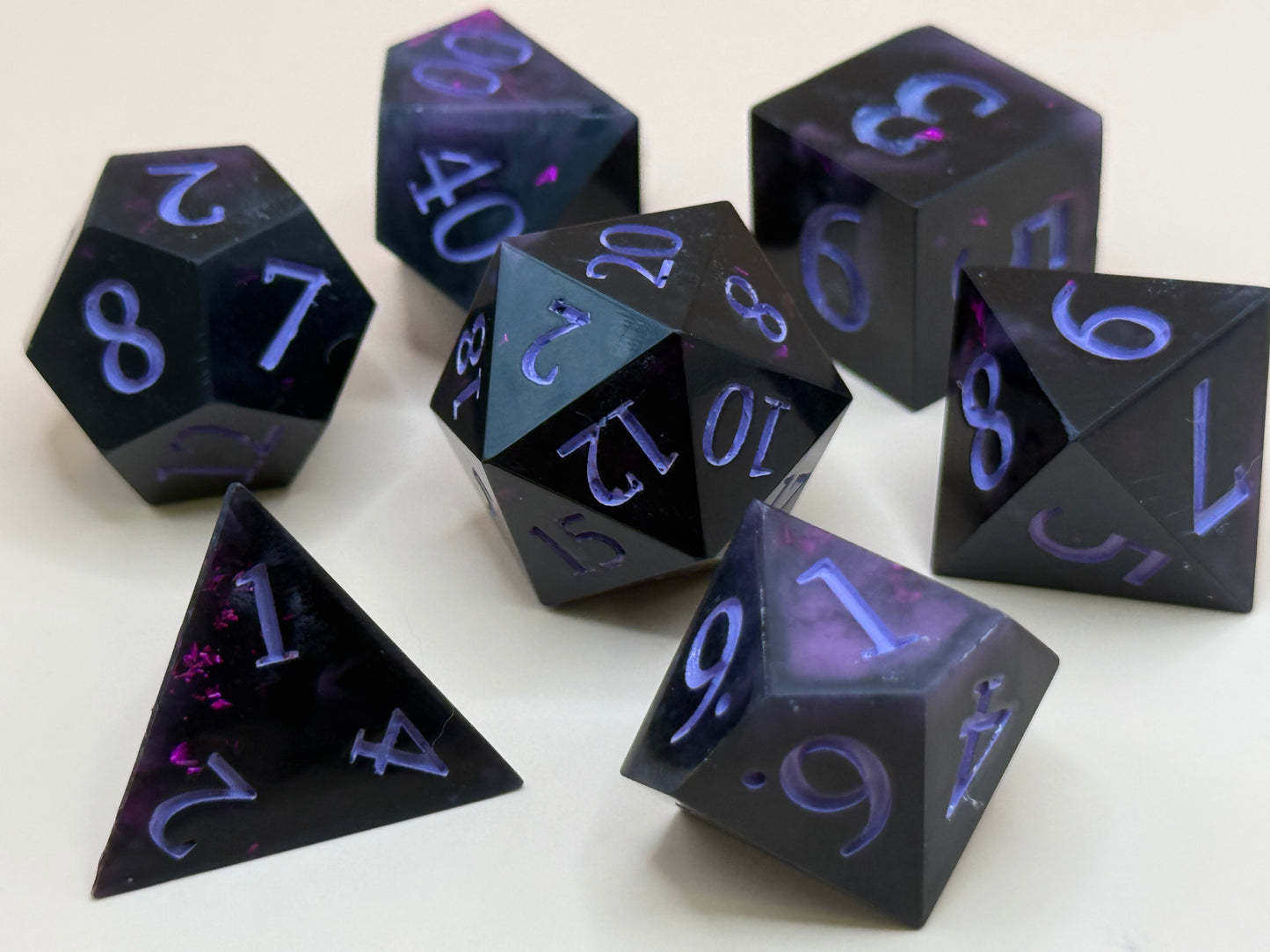 Set of black polyhedral dice with purple numbering on a white background
