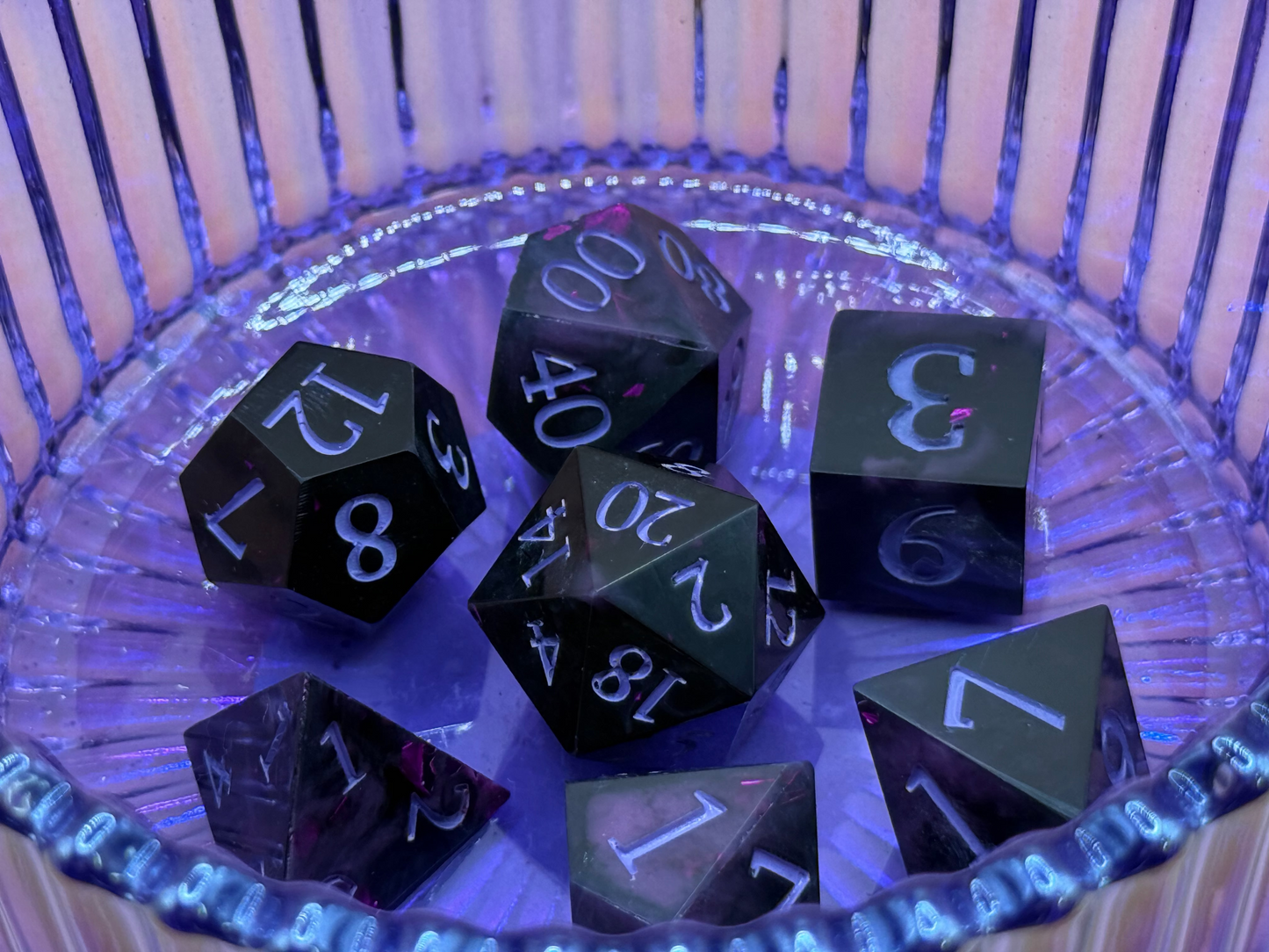Set of black polyhedral dice on a reflective surface with a purple hue