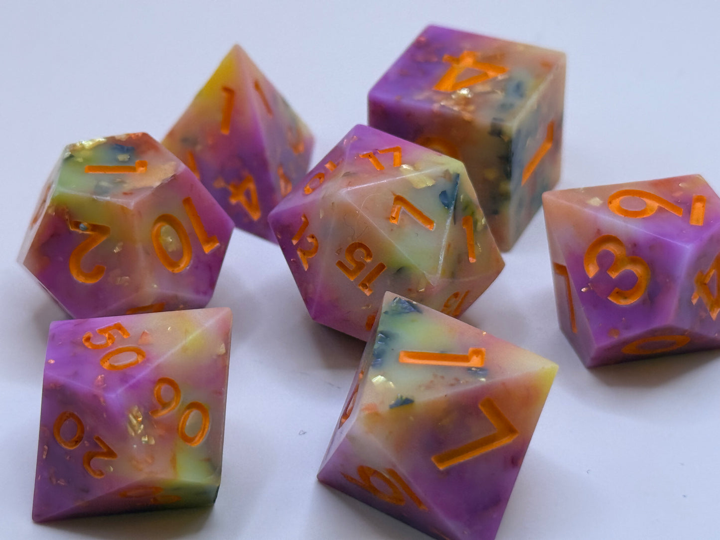 Set of colorful polyhedral dice with orange numbers on a white background