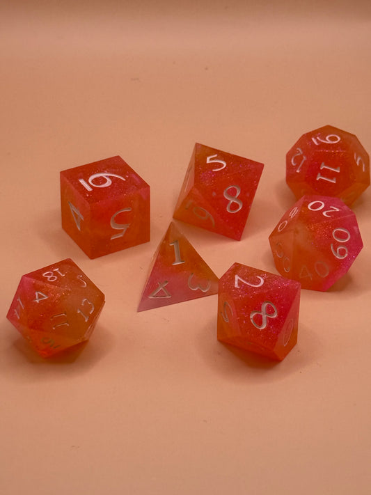 A set of seven, D&D hand-poured, resin dice in orange, pink and white on a wooden table. Numbers inked in white.