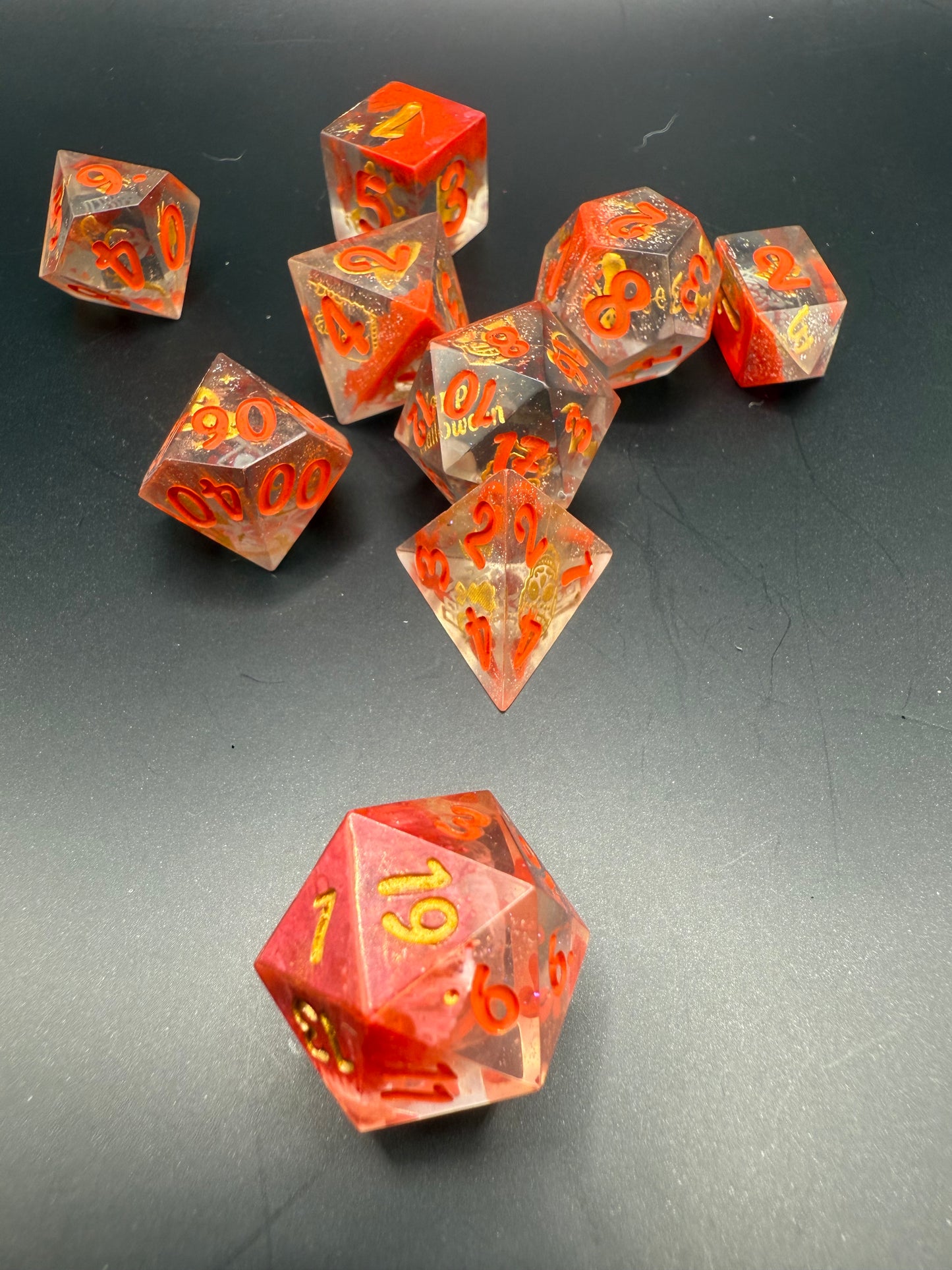 Set of red and clear dice with gold Halloween details and red numbers on a dark surface.