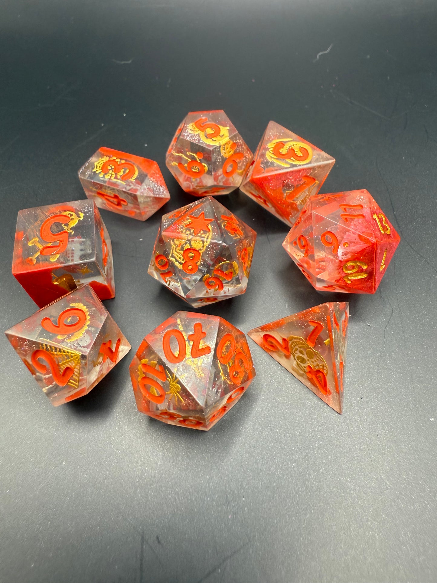 Set of red and clear dice with gold Halloween details and red numbers on a dark surface.