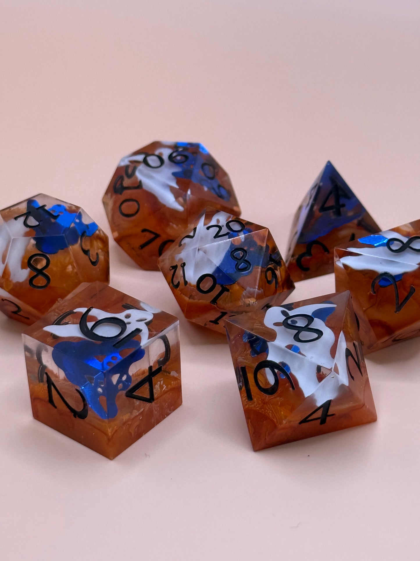 Orange sharp-sided, seven polyhedral dice with ghosts inside of them on a white surface.
