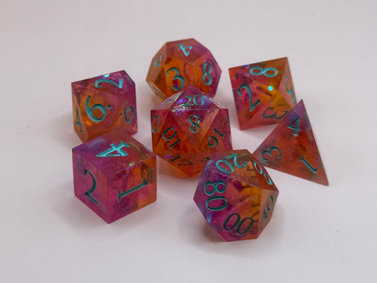 A set seven, D&D hand-poured, resin dice in orange, pink and white , with flecks of glitter, on a wooden table. Numbers inked in teal.