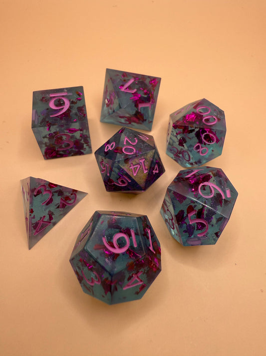 Transparent light blue sharp-edge resin dice with flecks of purple foil on a table.