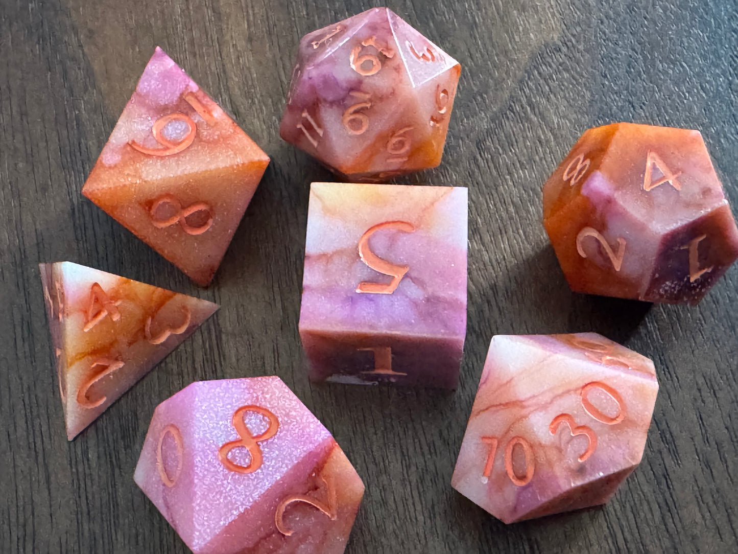 Orange, pink, and white, marbled sharp-edge hand-poured resin dice displayed on a table.