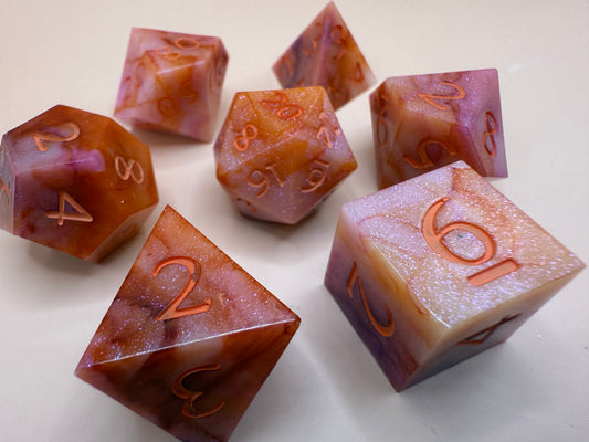 Orange, pink, and white, marbled sharp-edge hand-poured resin dice displayed on a white surface.
