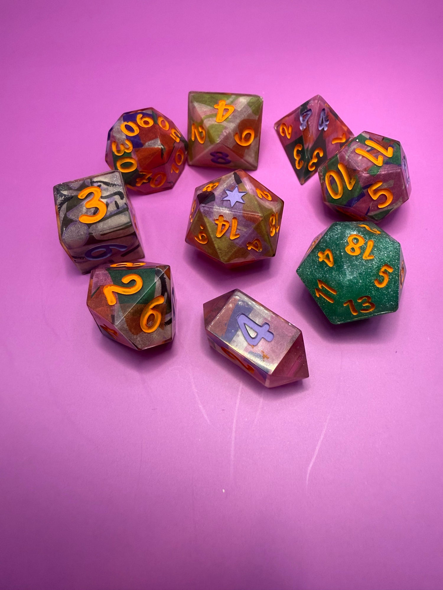 Colorful hand-poured polyhedral dice set with orange numbers on a pink background