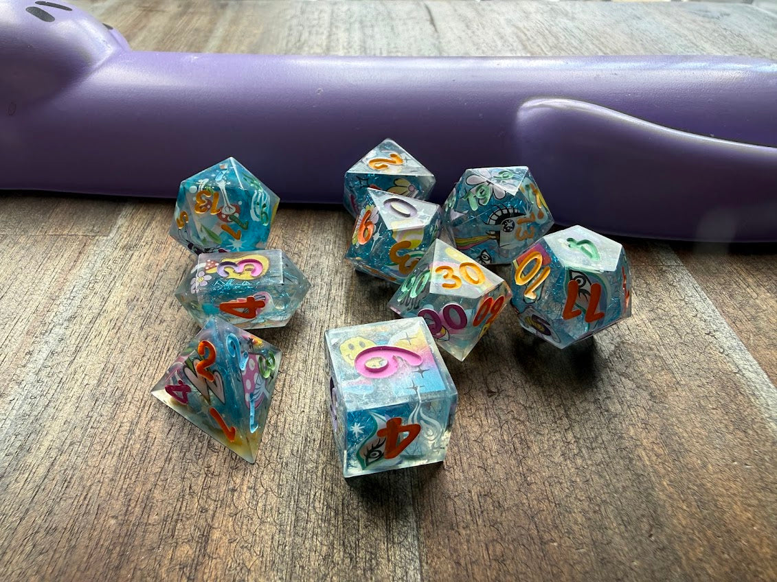 Set of colorful polyhedral dice on a wooden surface with a purple object in the background.