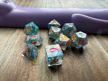 Set of colorful polyhedral dice on a wooden surface with a purple object in the background.