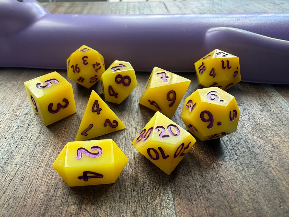 Yellow polyhedral dice set on a wooden surface with a purple object in the background.