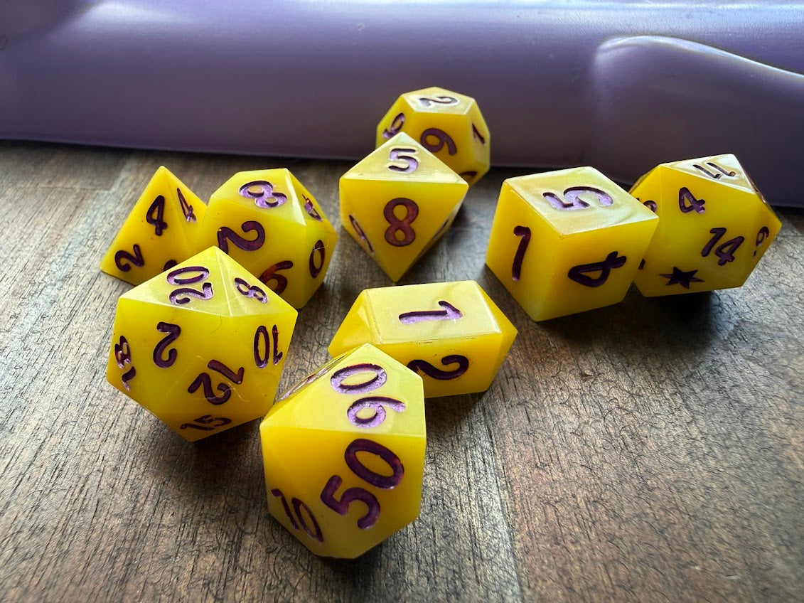 Yellow polyhedral dice with purple numbers on a wooden surface