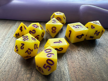 Yellow polyhedral dice with purple numbers on a wooden surface