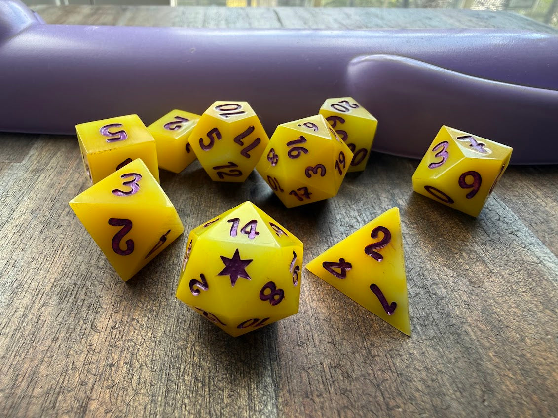 Yellow polyhedral dice set on a wooden surface with a purple object in the background.