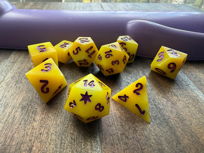 Yellow polyhedral dice set on a wooden surface with a purple object in the background.