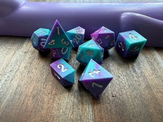 Set of polyhedral dice with purple and teal colors on a wooden surface.