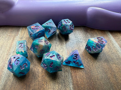 Set of colorful polyhedral dice on a wooden surface with a purple handle in the background.