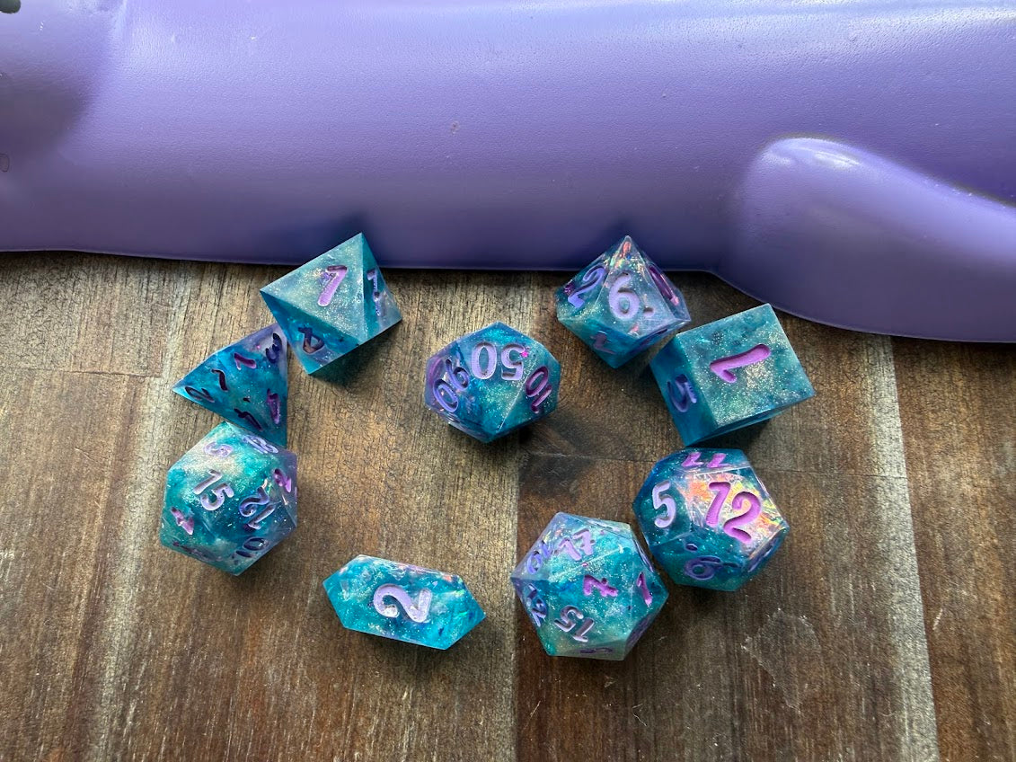 Set of teal polyhedral dice with purple numbers on a wooden surface