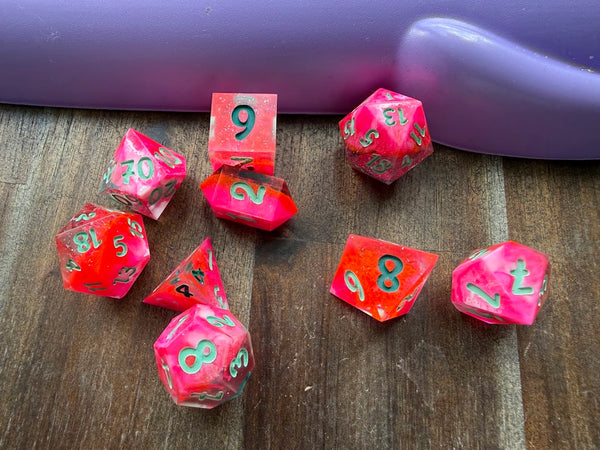 Set of colorful polyhedral dice on a wooden surface with a purple object in the background.