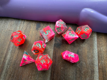Pink polyhedral dice on a wooden surface with a purple object in the background