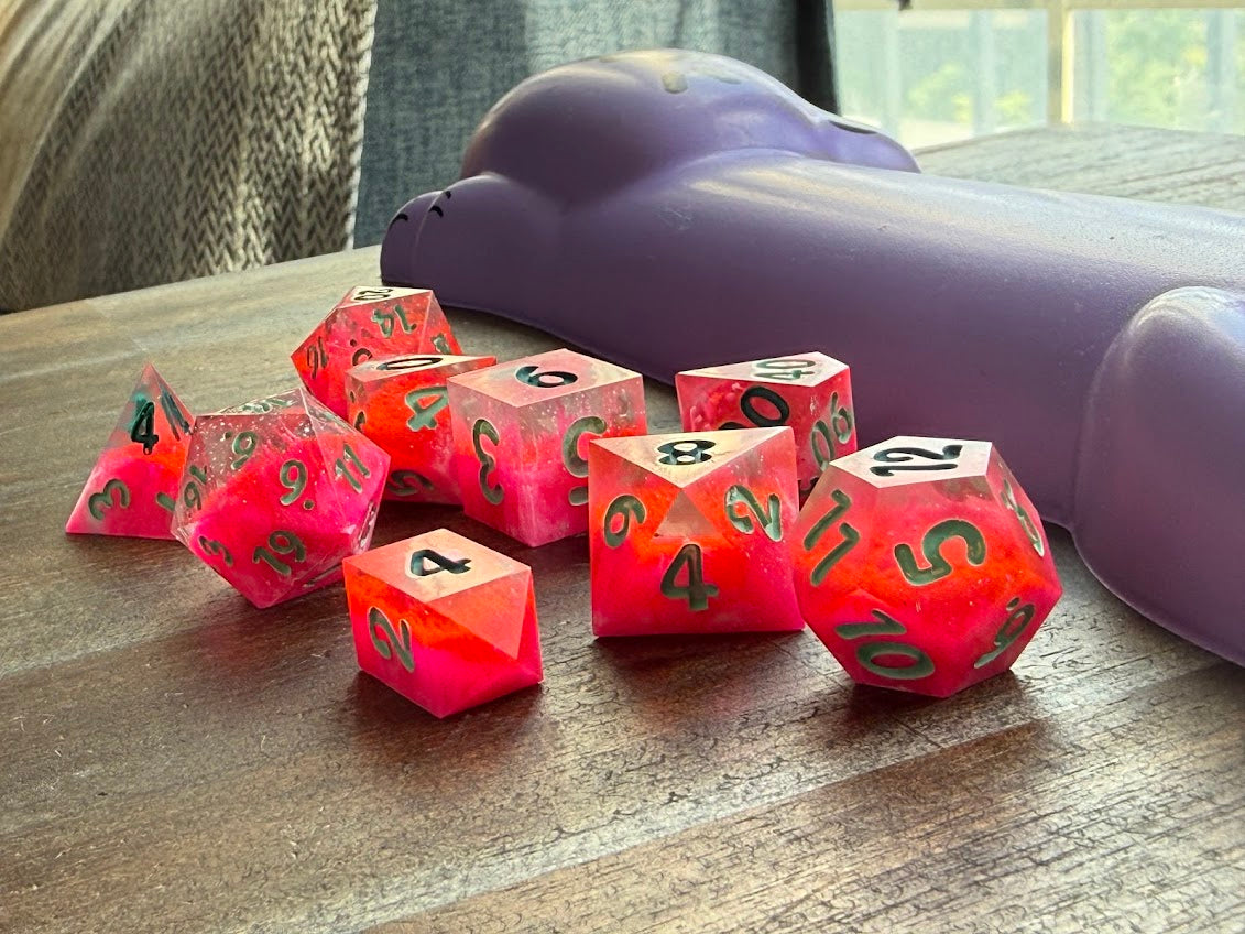 Red polyhedral dice with black numbers on a wooden surface, with a purple object in the background.