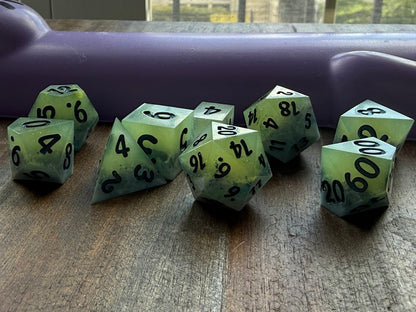 Set of green polyhedral dice with black numbers on a wooden surface