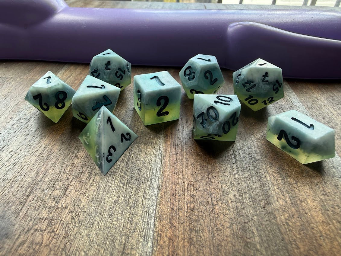Set of green polyhedral dice with black numbers on a wooden surface