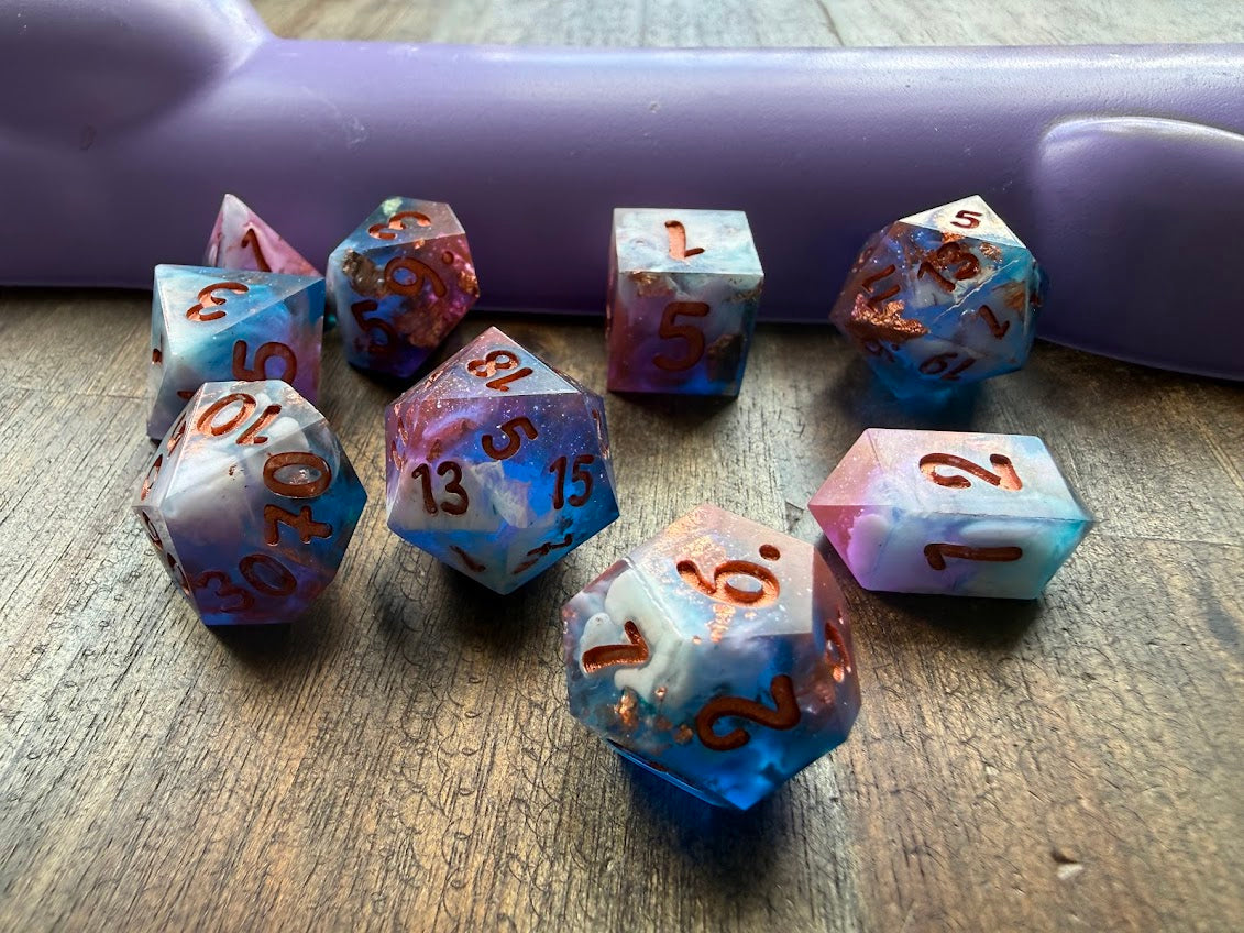 Set of colorful polyhedral dice on a wooden surface with a purple object in the background.