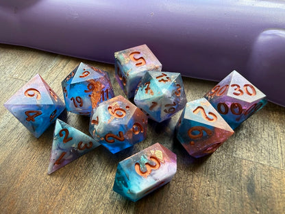 Set of colorful polyhedral dice on a wooden surface with a purple object in the background.