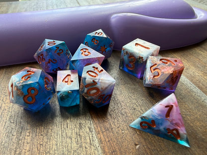 Set of colorful polyhedral dice on a wooden surface with a purple object in the background.