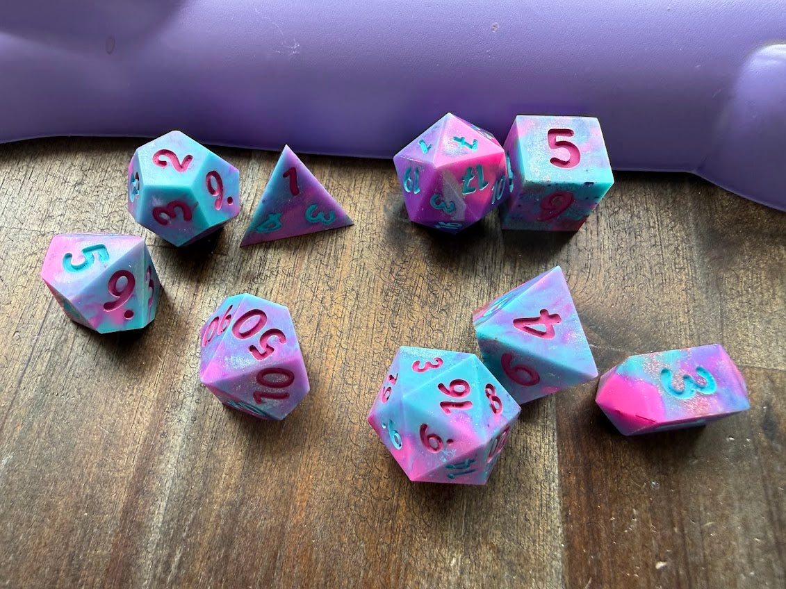 Set of colorful polyhedral dice on a wooden surface with a purple container in the background.