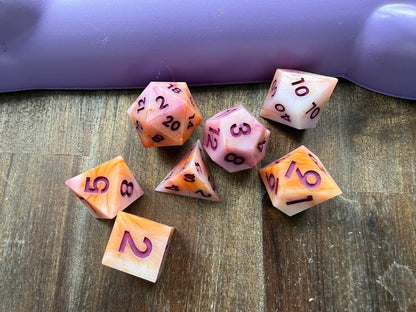Set of colorful polyhedral dice on a wooden surface with a purple object in the background.