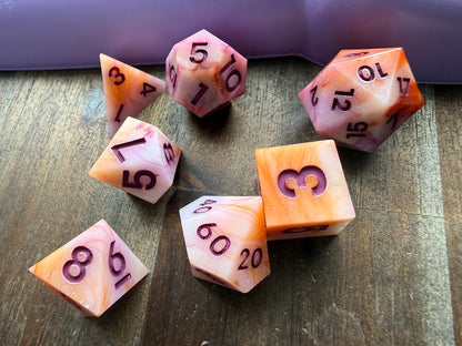 Set of pink and orange polyhedral dice on a wooden surface