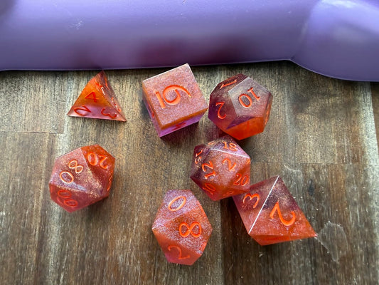 Set of red polyhedral dice on a wooden surface with a purple cylindrical object in the background.