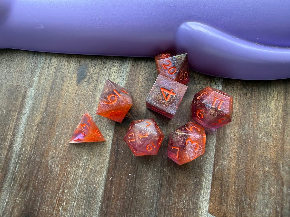 Set of red polyhedral dice on a wooden surface with a purple cylindrical object in the background.