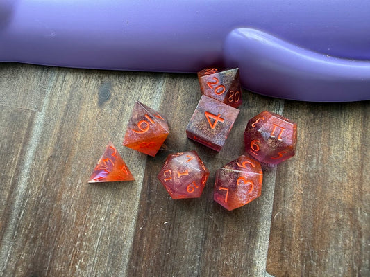 Set of red polyhedral dice on a wooden surface with a purple cylindrical object in the background.
