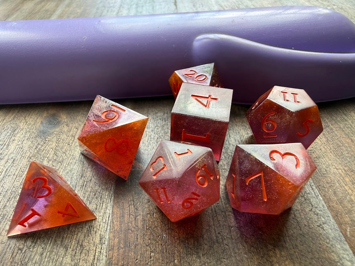 Set of red polyhedral dice on a wooden surface with a purple cylindrical object in the background.